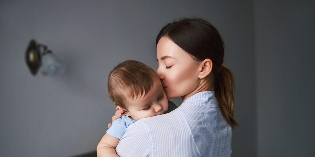 Beautiful mother caressing her little boy and kissing while lulling for daytime sleep