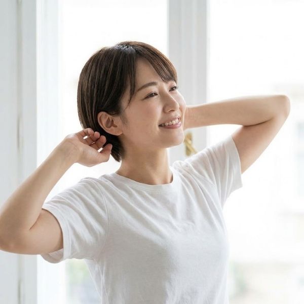 A smiling individual completes a gentle morning stretch near a large, bright window.